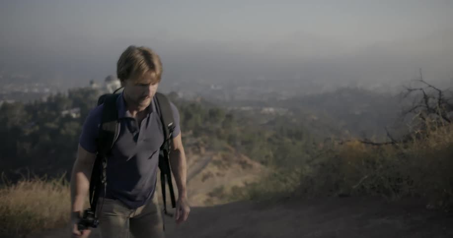 A man walks uphill holding a camera