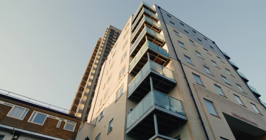 A contrast between old and new housing styles in a city with a towering concrete block of flats next to a modern apartment building with balconies