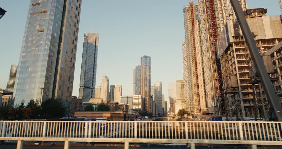 Modern skyscrapers in west india dock are seen from a moving vehicle partially blocked by a dark bridge support pillar and railing