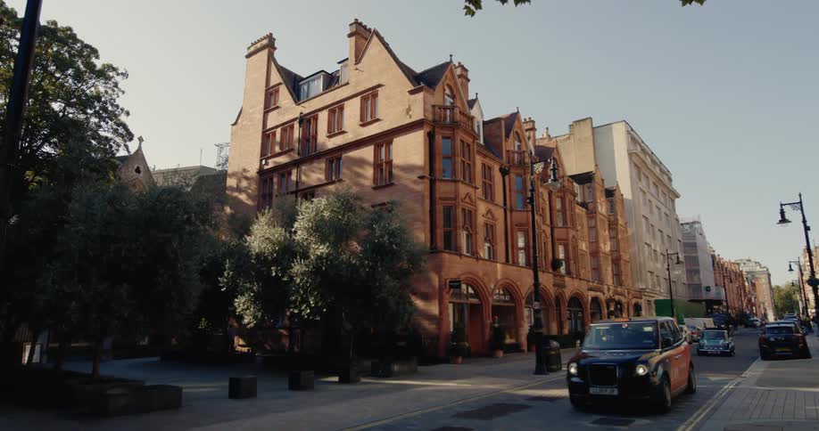 A row of brick buildings with arched windows and cars driving down a street lined with trees