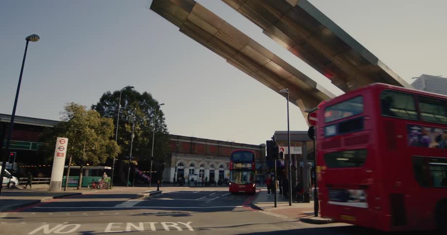 Red doubledecker london bus leaves a station near a metro entrance with modern angular architecture