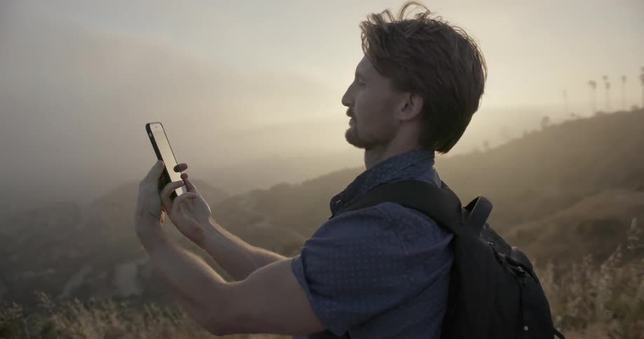 A man is using a phone as he stands on a mountain