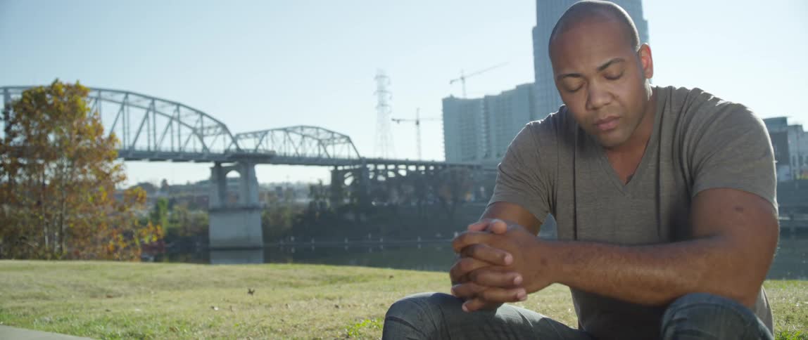 Man sits down with his hands folded with a large building in the background