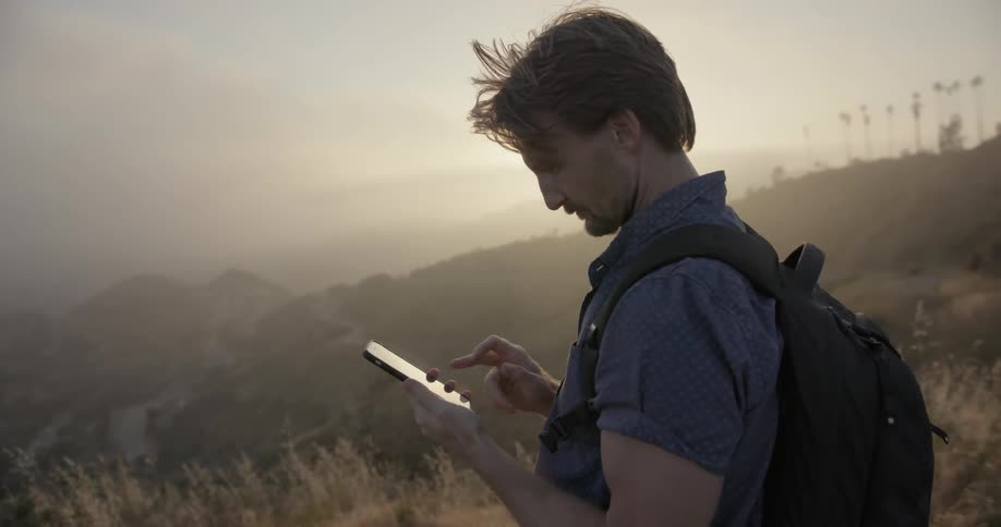 A man scrolls on his phone in a hilly area