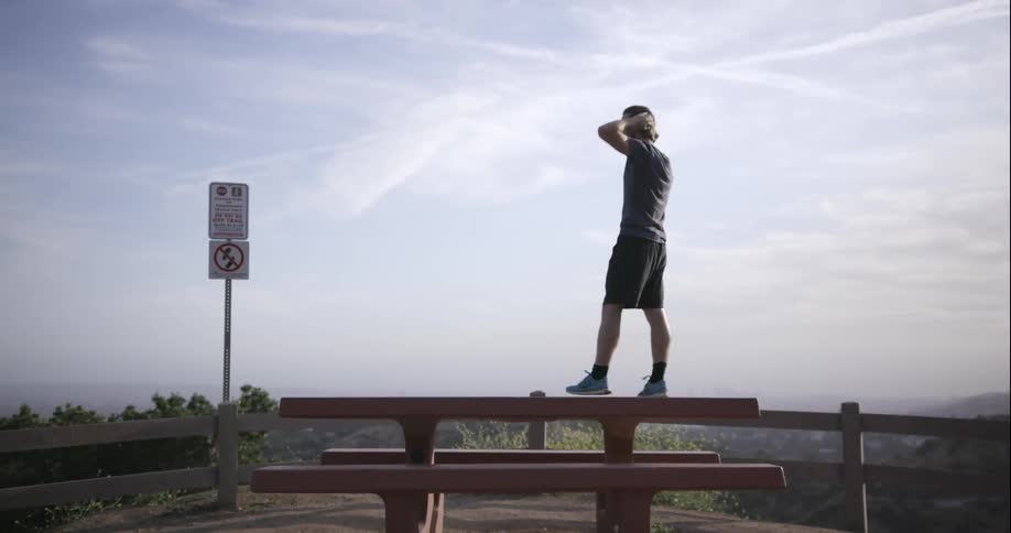 A man stands on top of a picnic table overlooking a valley