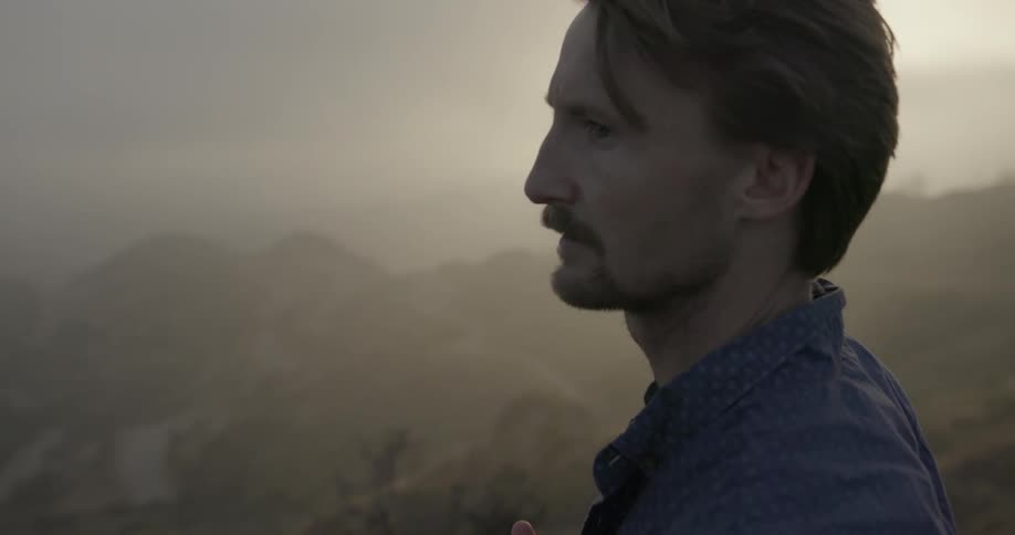 A man is standing on a hillside looking around on a hazy day