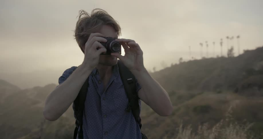 A man is using a camera to take photos in a hilly area on a hazy day