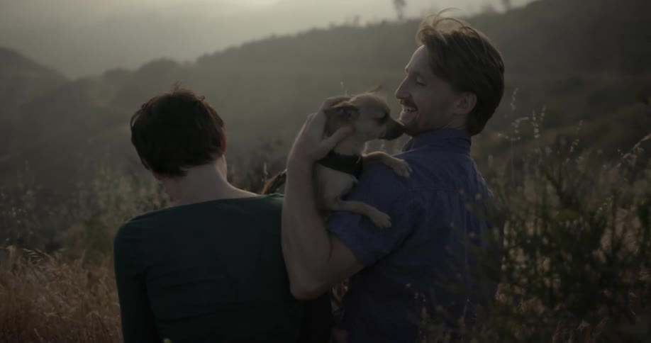 A man and woman sit with a chihuahua on a hillside