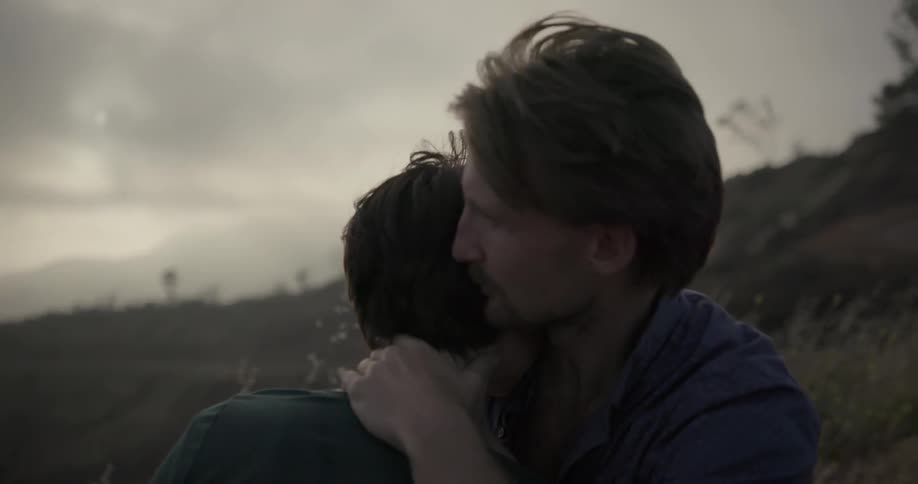A man and woman sitting on a hillside are embracing