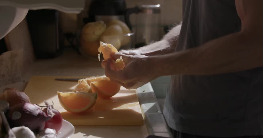 A man peels and sections an orange in the kitchen