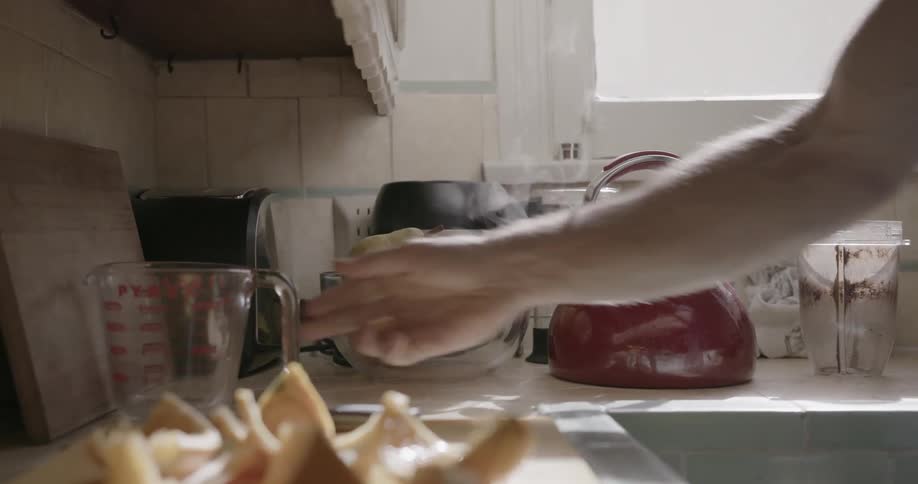 A man sets a cup on a counter and flips the lid on a steaming kettle