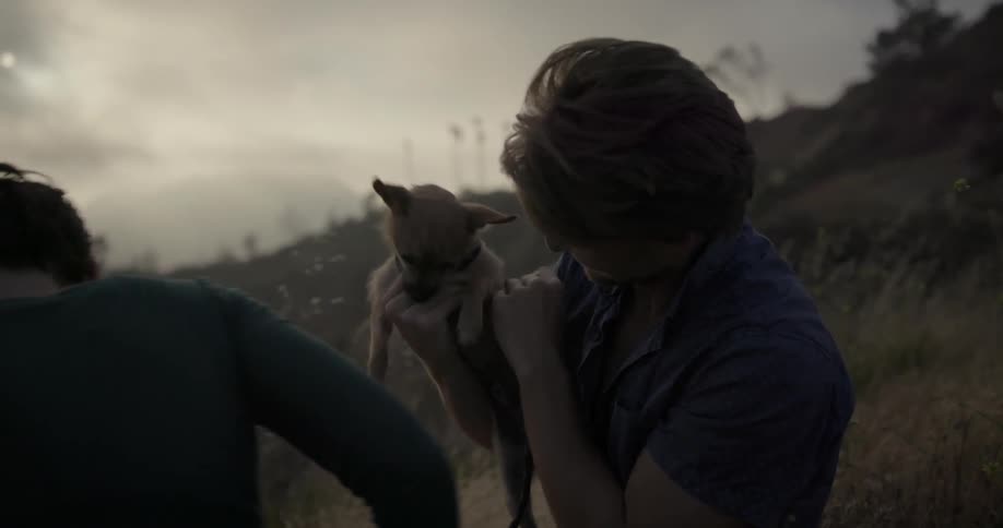 A man and woman sit in the hills with a chihuahua
