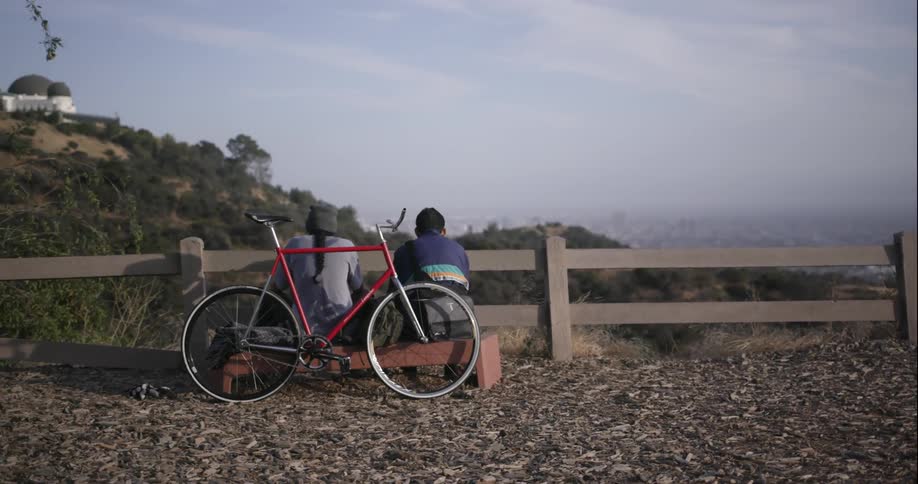 Two people sit on a bench with a bicycle parked against it