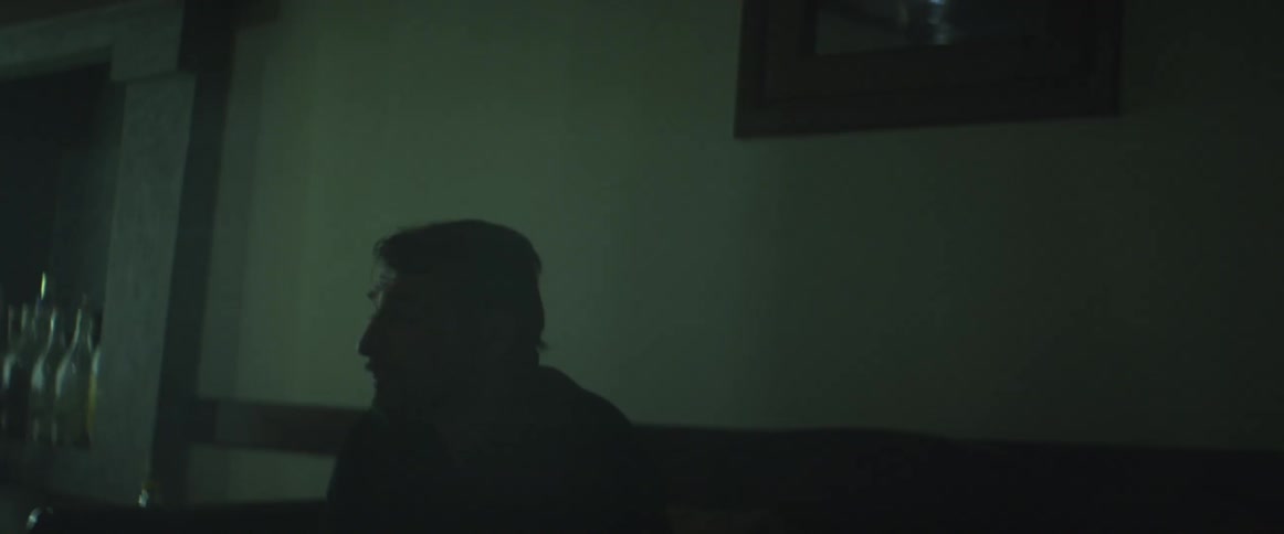 A man sits in the dark on a sofa and drinks from a bottle alone