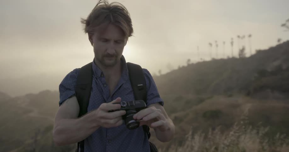 A man is using a camera to take photos in a hilly area on a hazy day