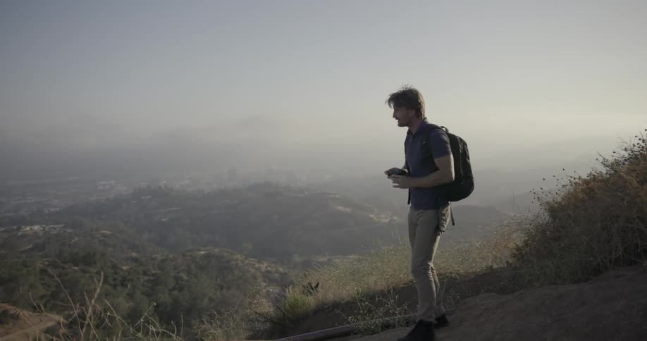 Man wearing a backpack takes pictures on top of a hill