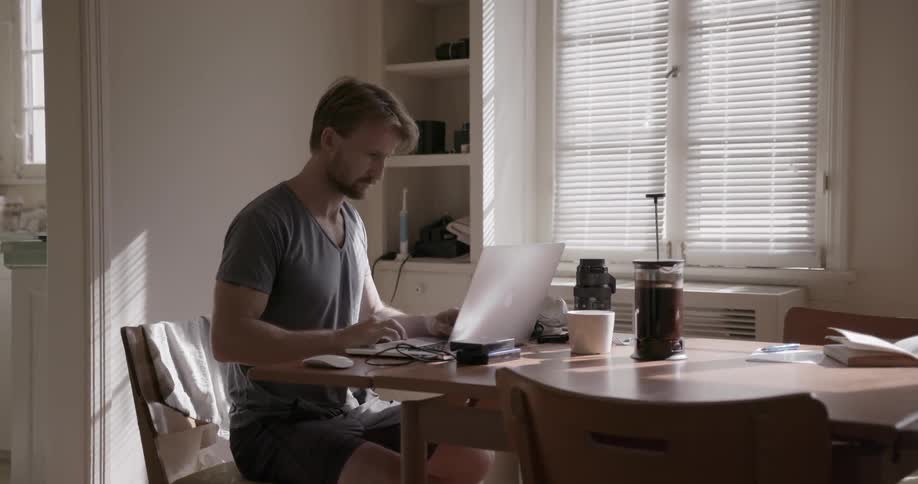 A man is sitting in his house and looking at a laptop at the table