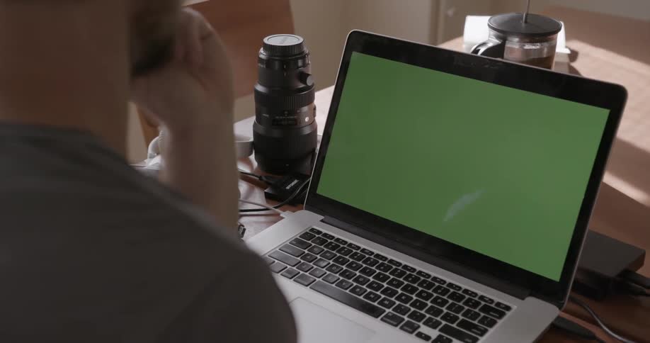 A man sits at a desk in front of a green screen