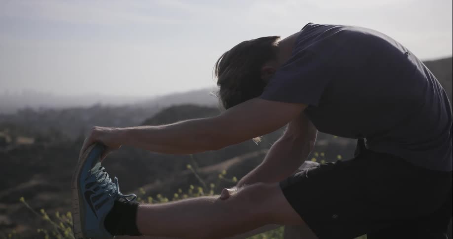 A man is stretching out his legs on a hiking trail