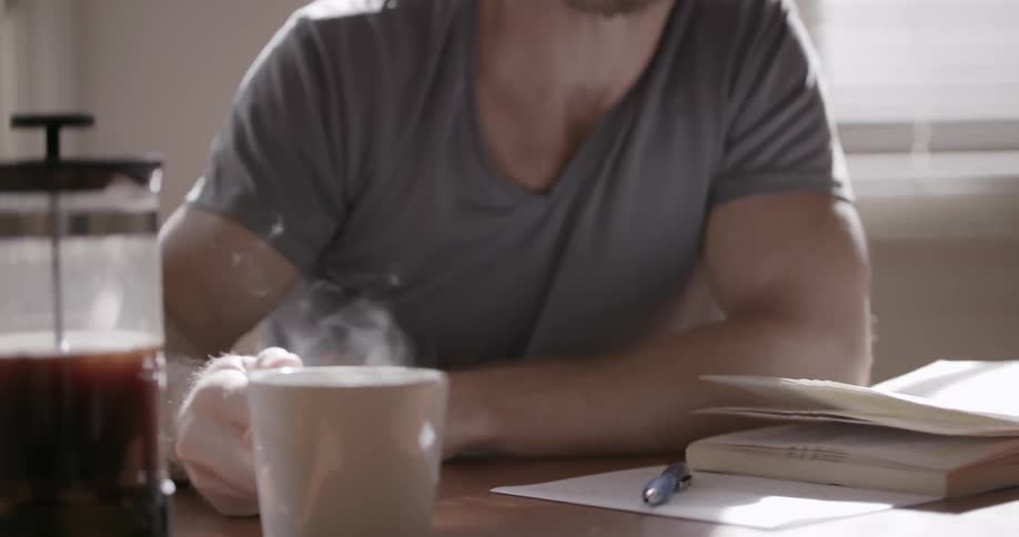 Man takes a drink out of a hot cup of coffee while sitting at a desk