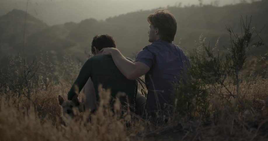 A man and woman are sitting together with a dog in a field