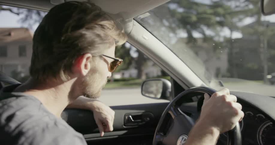 A man in sunglasses is driving a car through a residential area