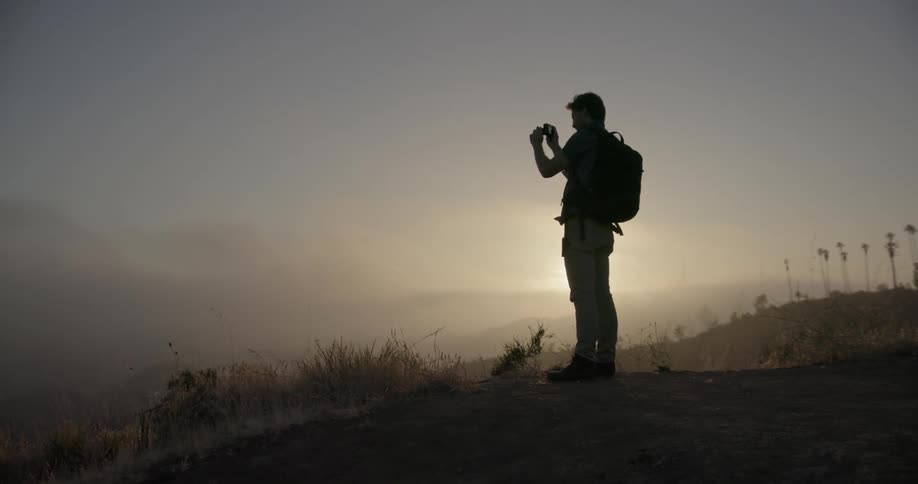 A man is taking a picture on top of a hillside