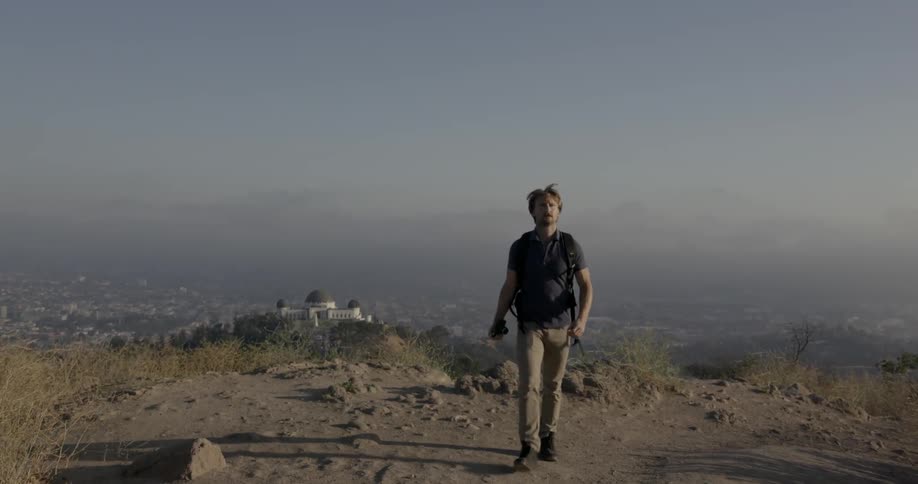 A man is hiking up a hill above a sprawling urban area