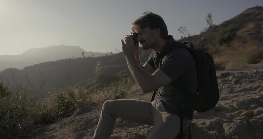 A man sits in the hills and takes a photograph