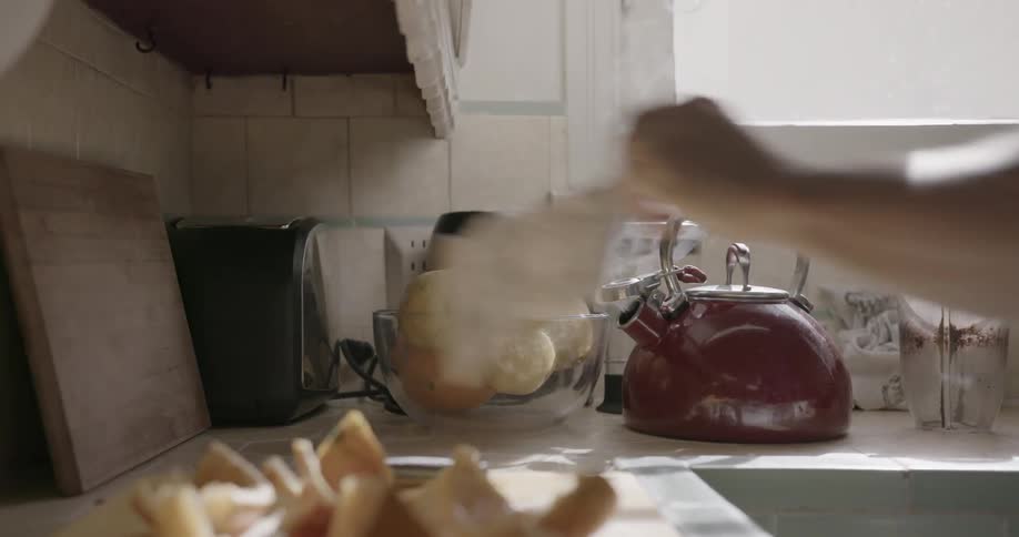 A man prepares food in a kitchen with a steaming kettle on the counter