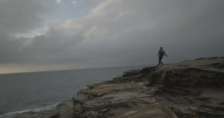 A man throwing something from an ocean-side cliff on a very cloudy day