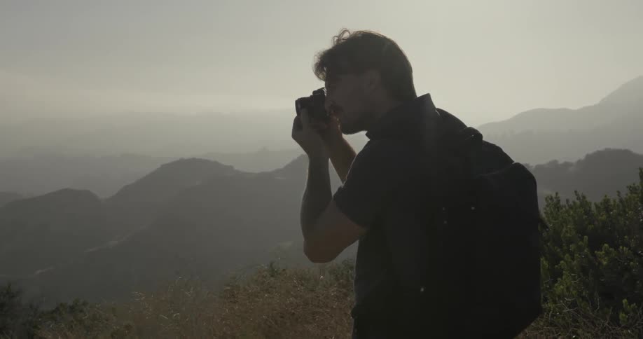 A man is using a camera to take photos in a hilly area on a hazy day