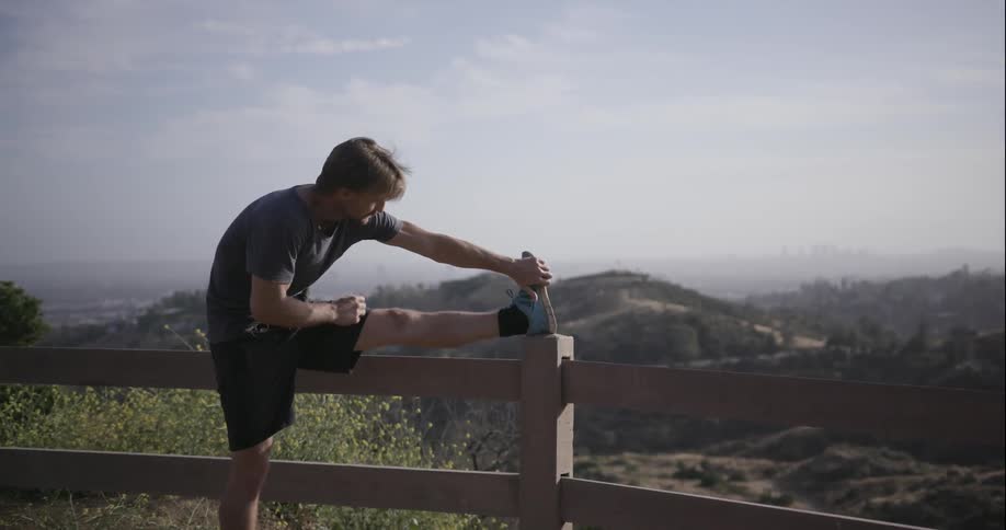 Man stretches leg on a fence post