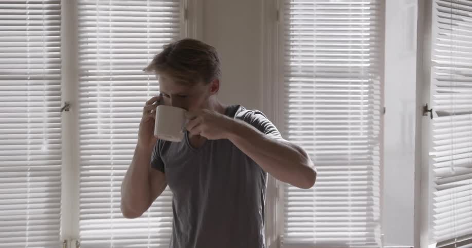 A man talks on the phone and takes a drink from a mug