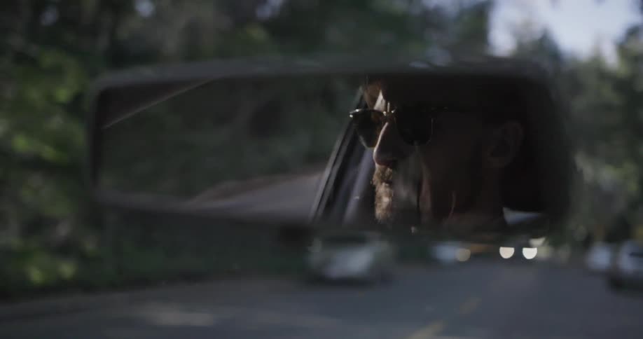A person can be seen driving a car in the rearview mirror