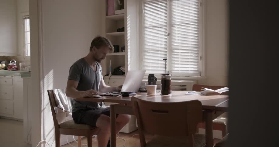 A man works on a laptop at a dining room table
