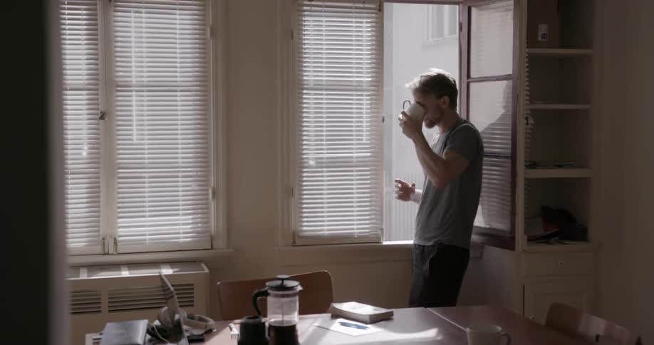 A man holds a coffee mug looking out the window