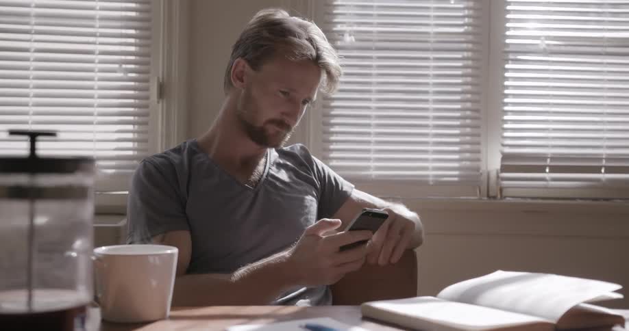 A man browses on his phone while sipping from a mug