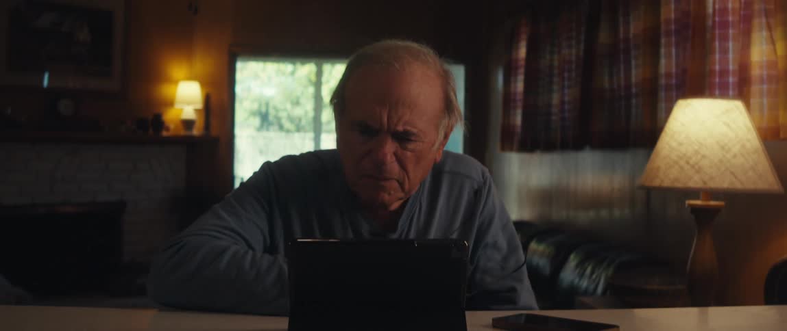 Elderly man taking off his glasses while sitting in front of a tablet
