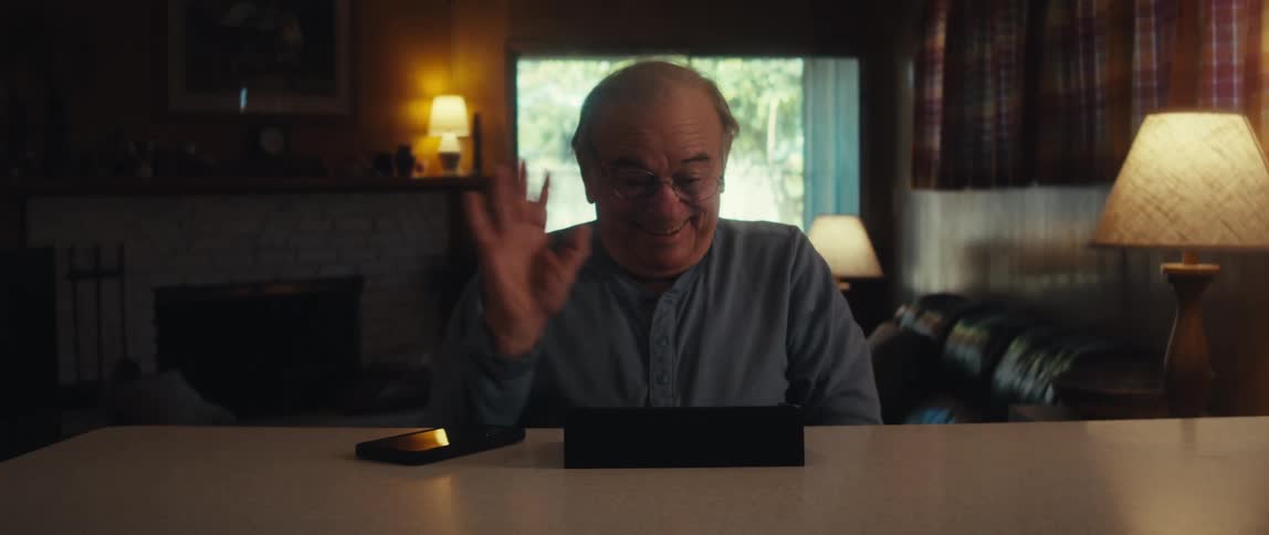 Elderly man sitting making a hand sign in front of a tablet