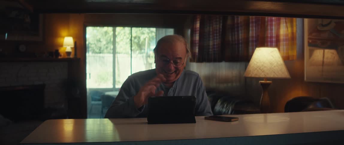 Elderly man making hello sign with one hand in front of a tablet on the table