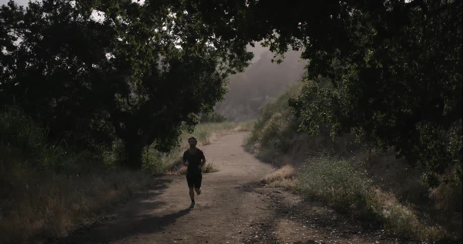 A man is running down a dirt trail in the shade
