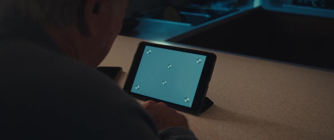 Elderly man wearing a blue shirt looks down at tablet screen