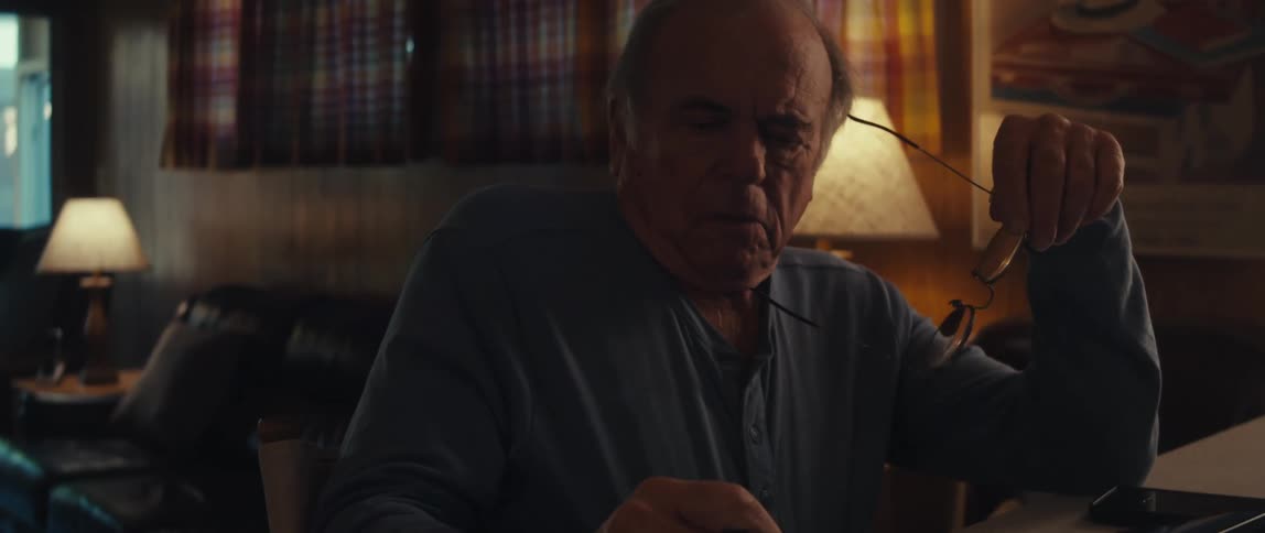 Elderly man sitting interacting with a calculator and taking off his glasses