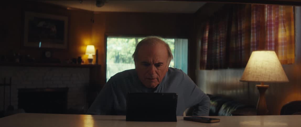 Elderly man sitting at the table and looking focused and scared at a tablet