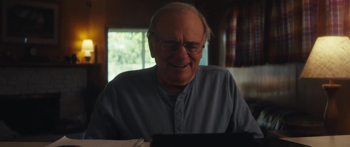 Elderly man with happy facial expression sitting at a table interacting with a tablet