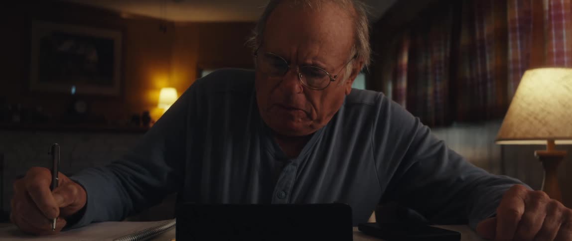 Elderly man sitting writing next to a tablet