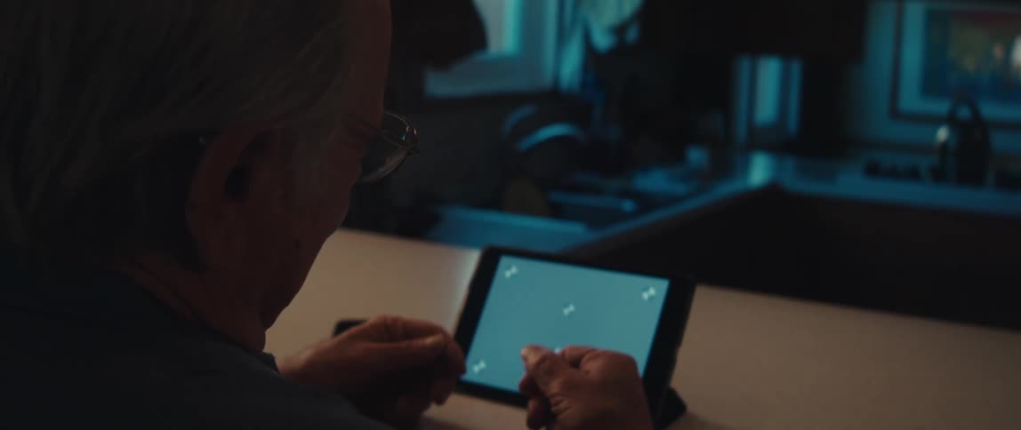 Elderly man with glasses sitting interacting with a tablet