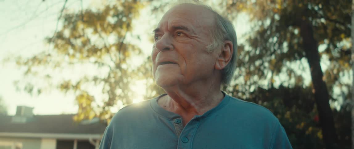 Elderly man holding smartphone while standing outdoors under trees