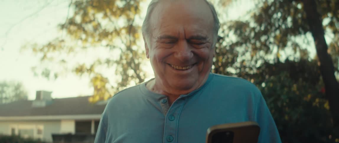 A man is tapping his phone and smiling in the yard